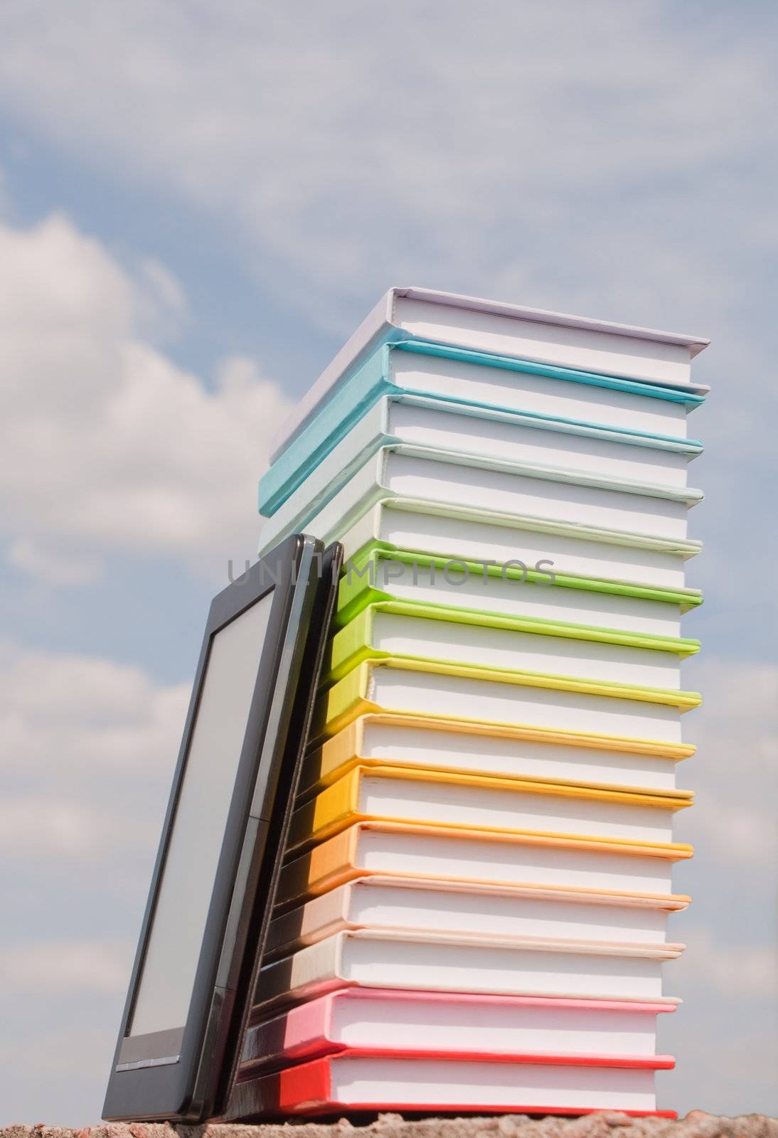 Stack of colorful books and electronic book reader outdoors by AndreyKr