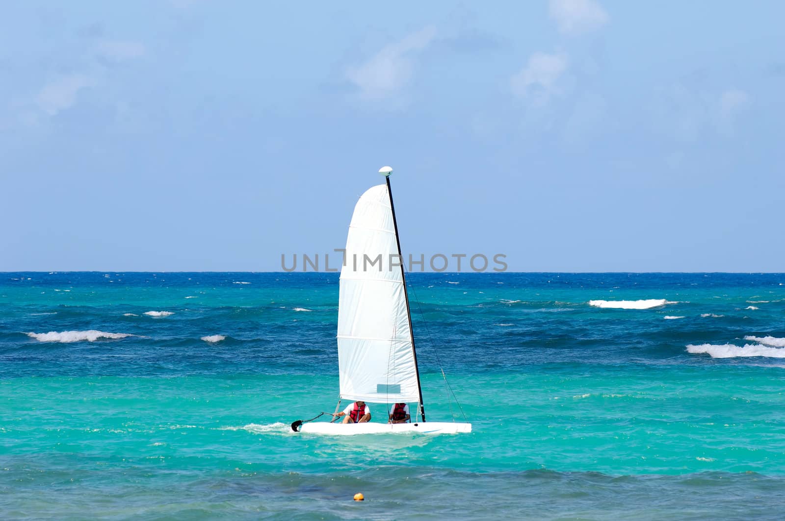 A sailboat is sailing on the blue caribbean sea.