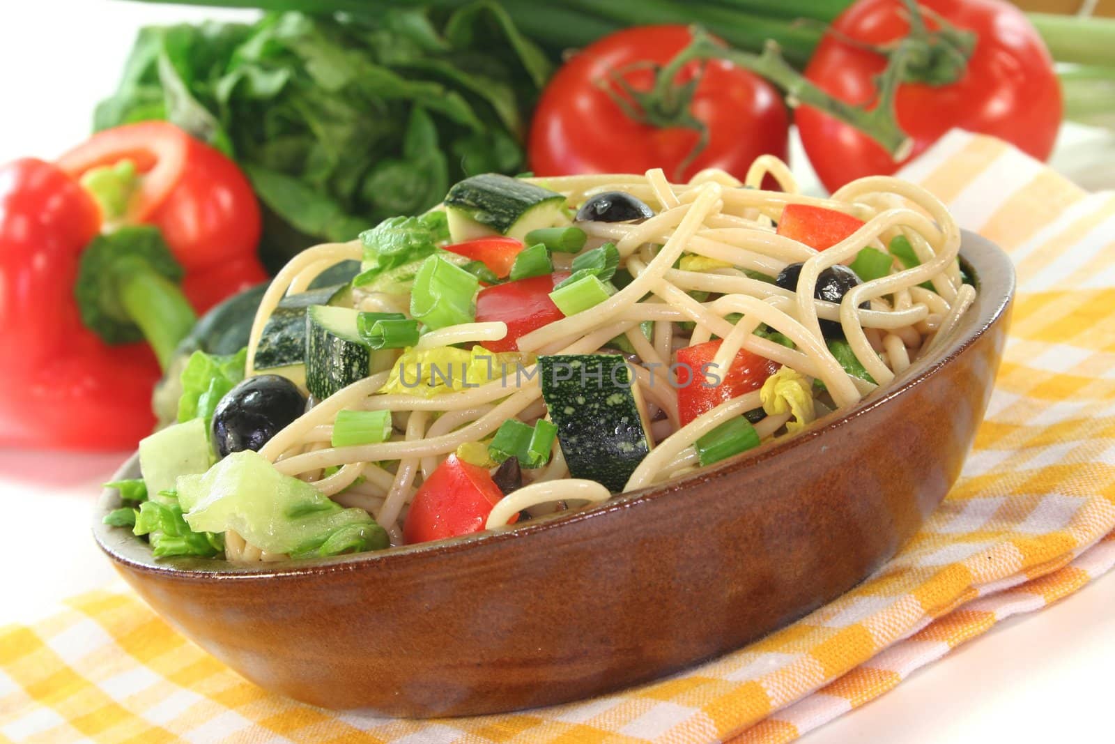 Spaghetti salad with lettuce, peppers, zucchini, olives, and green onions on a white background