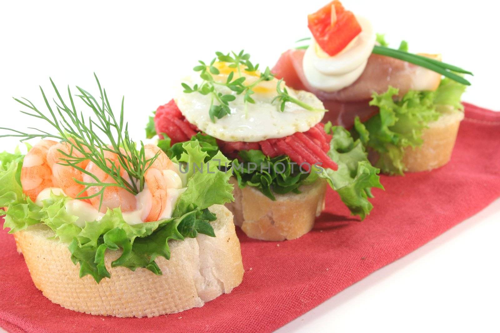 Canape with lettuce, ham, steak tartare, shrimp and quail eggs on a white background