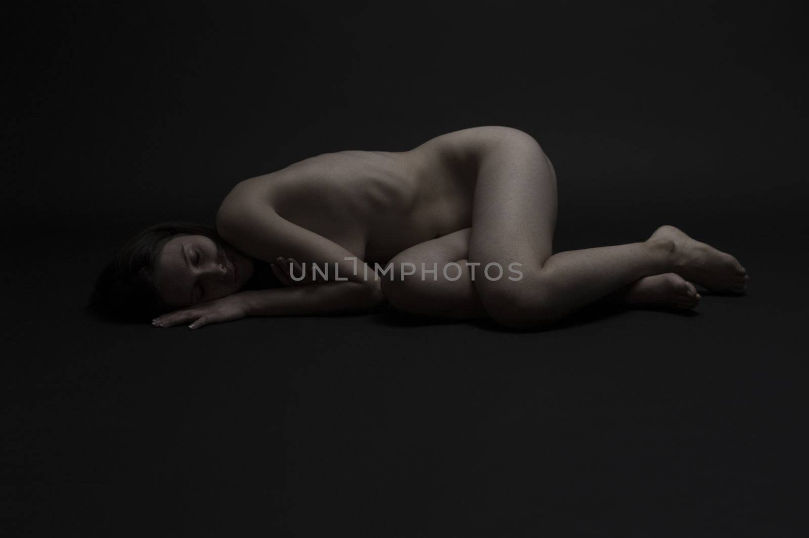 Low-key studio portrait of a naked young woman resting