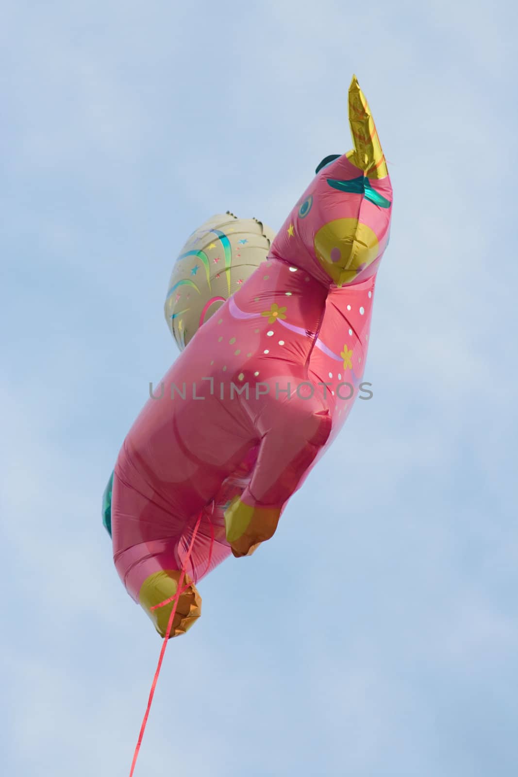 Floating pink baloon on a red string against blue sky