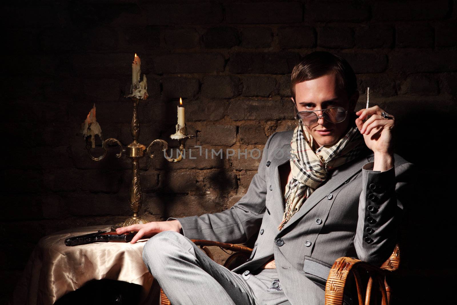 Mafioso. Man with a gun in a wicker chair on the background of an old brick wall

