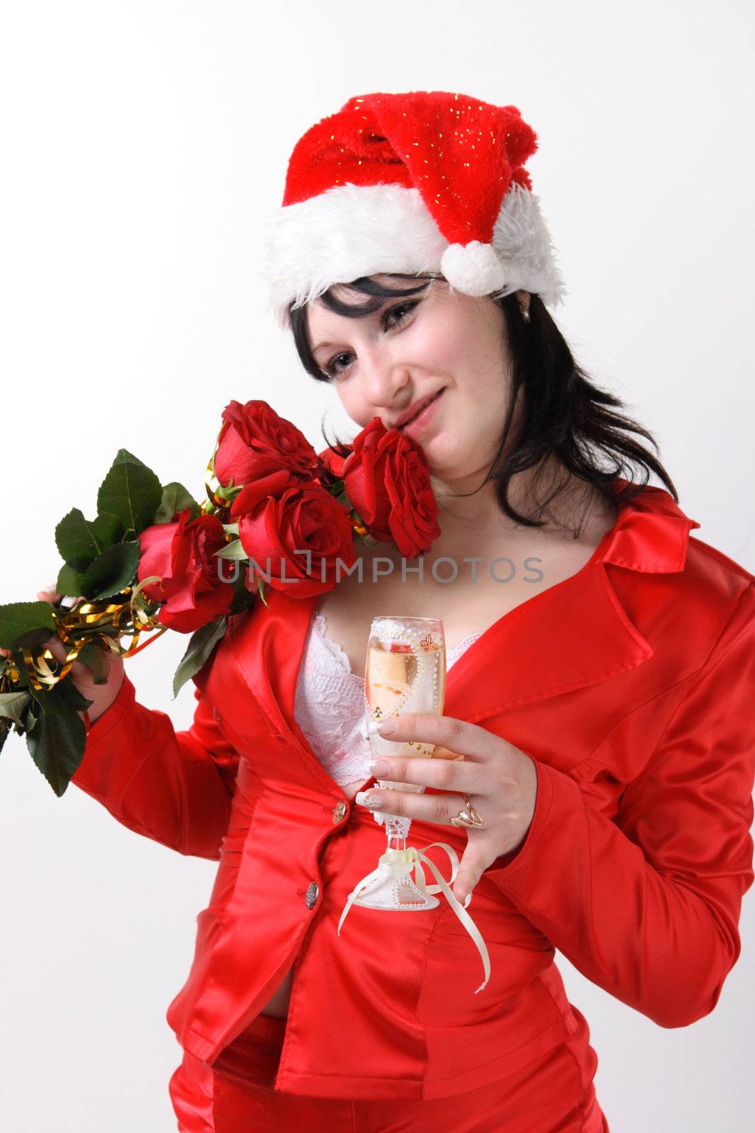 Portrait of a beautiful young woman in a red suit and hat of Santa Claus with red roses and champagne on the grey background
