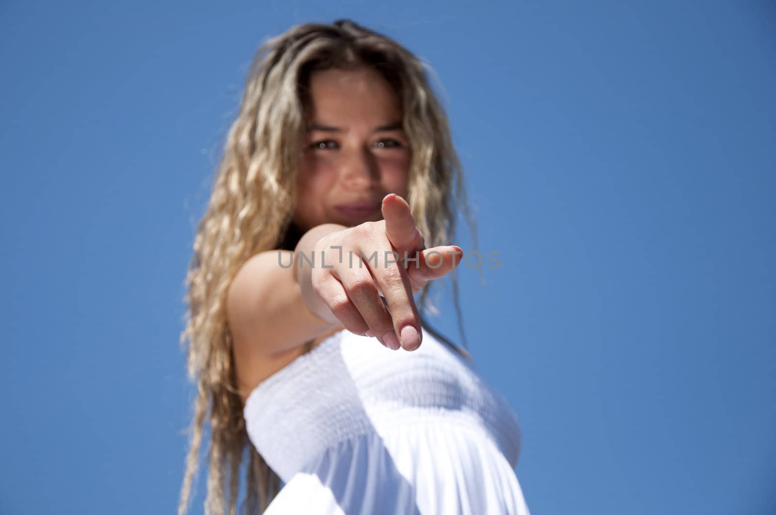 Portrait of the young woman pointing a finger against the blue sky