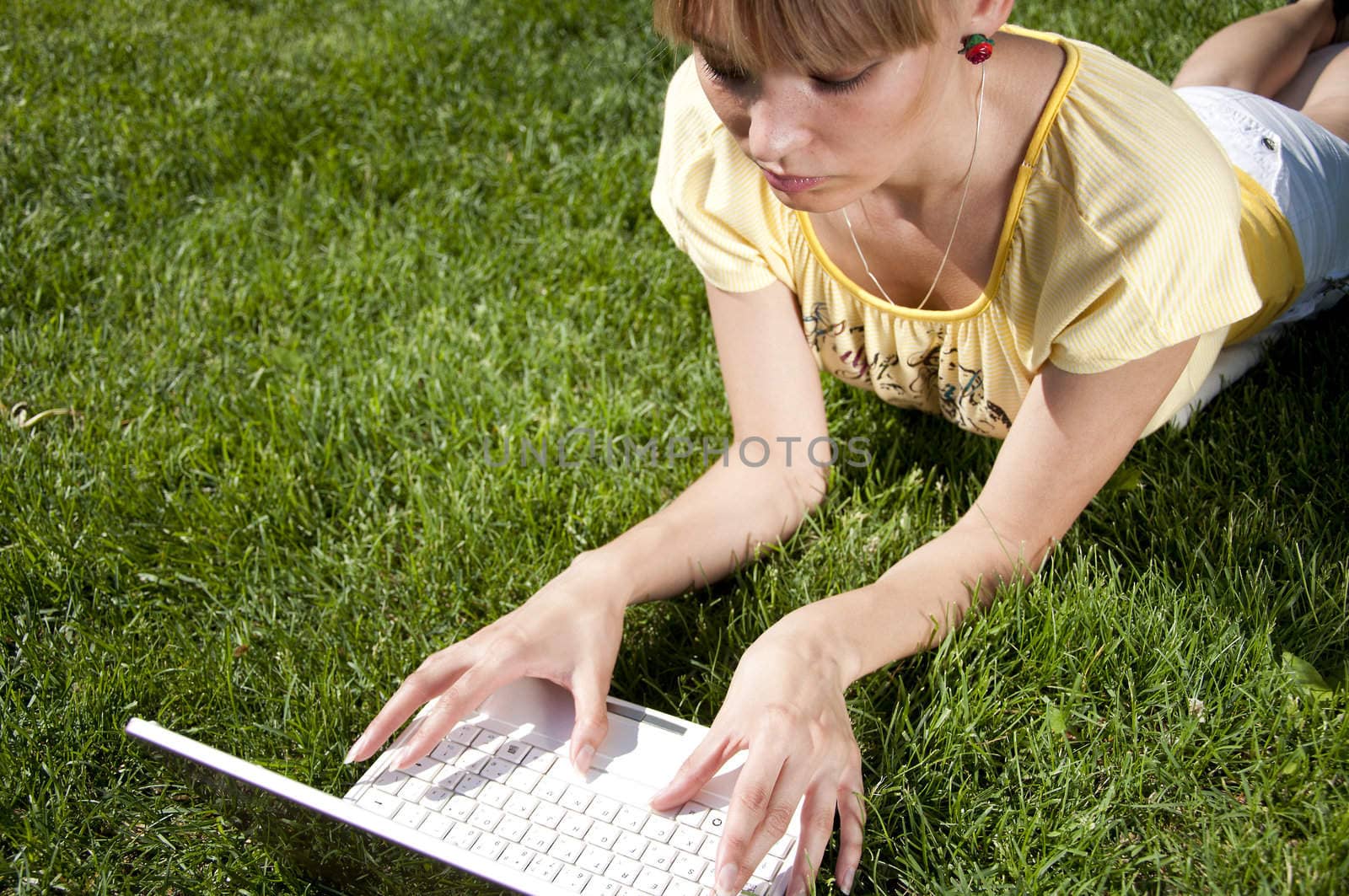 Young woman with laptop sitting on green grass in the park