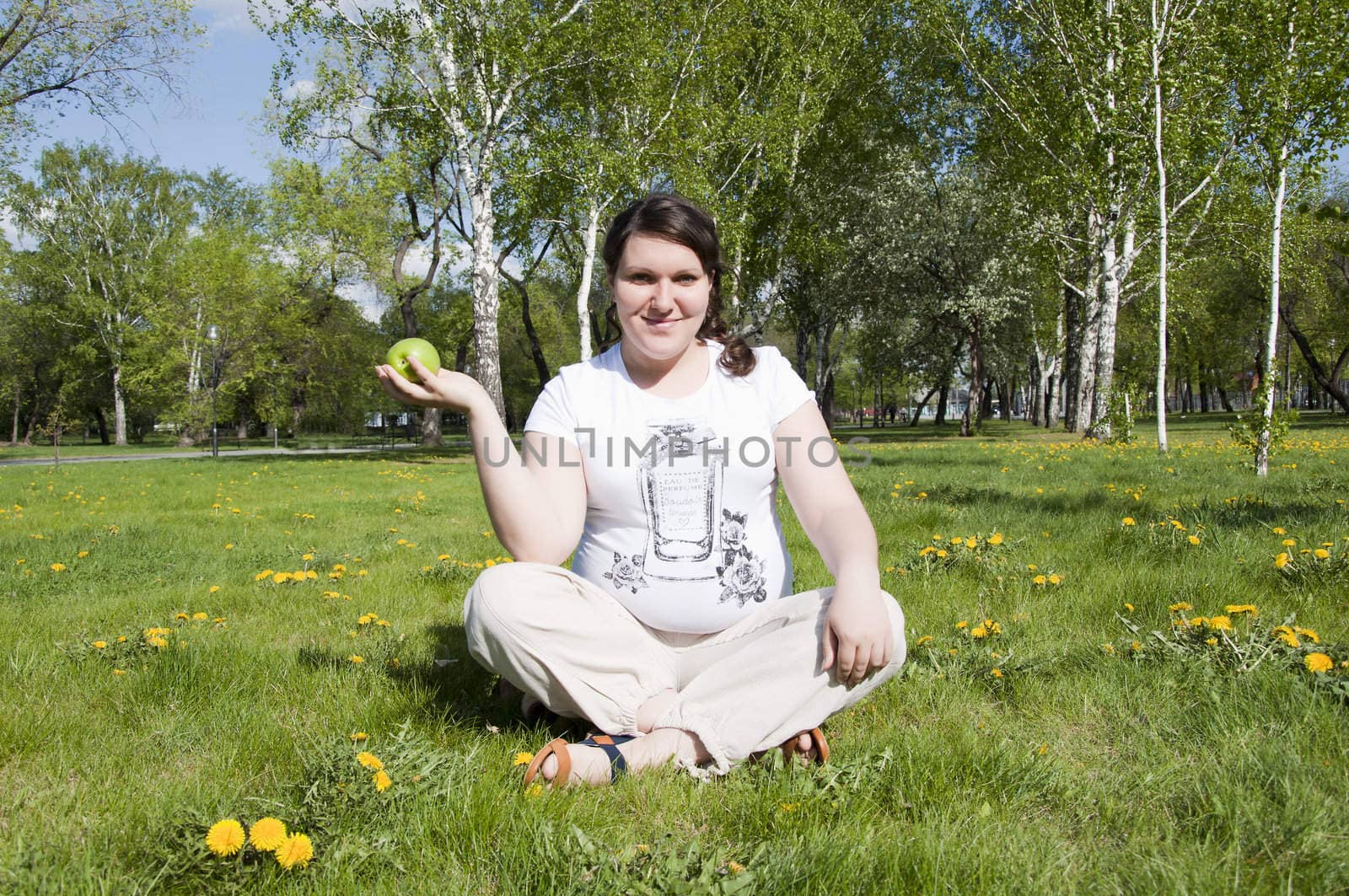 woman sitting on the grass in the park with an apple