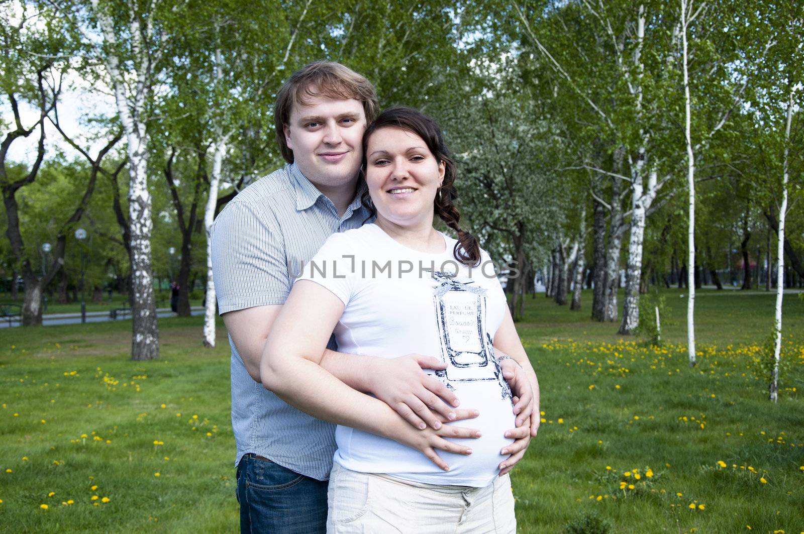 man hugs pregnant woman in the park