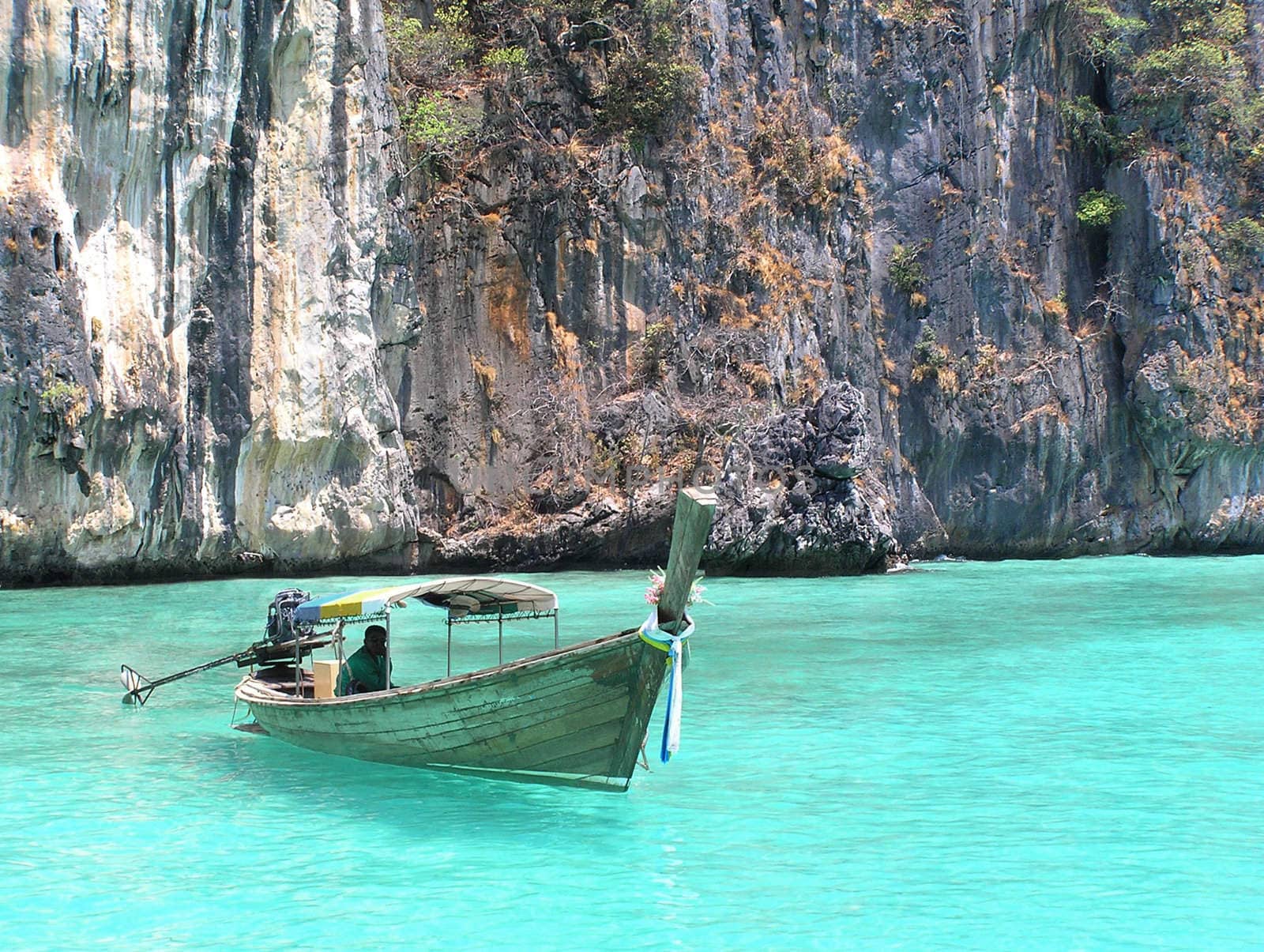 Boat in clear blue water with rocks in background.