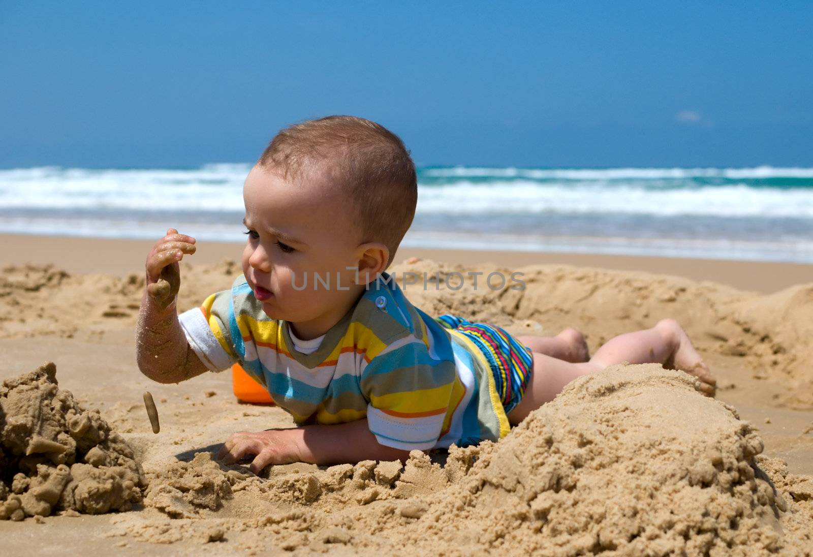 One year old boy lying down playing with sand