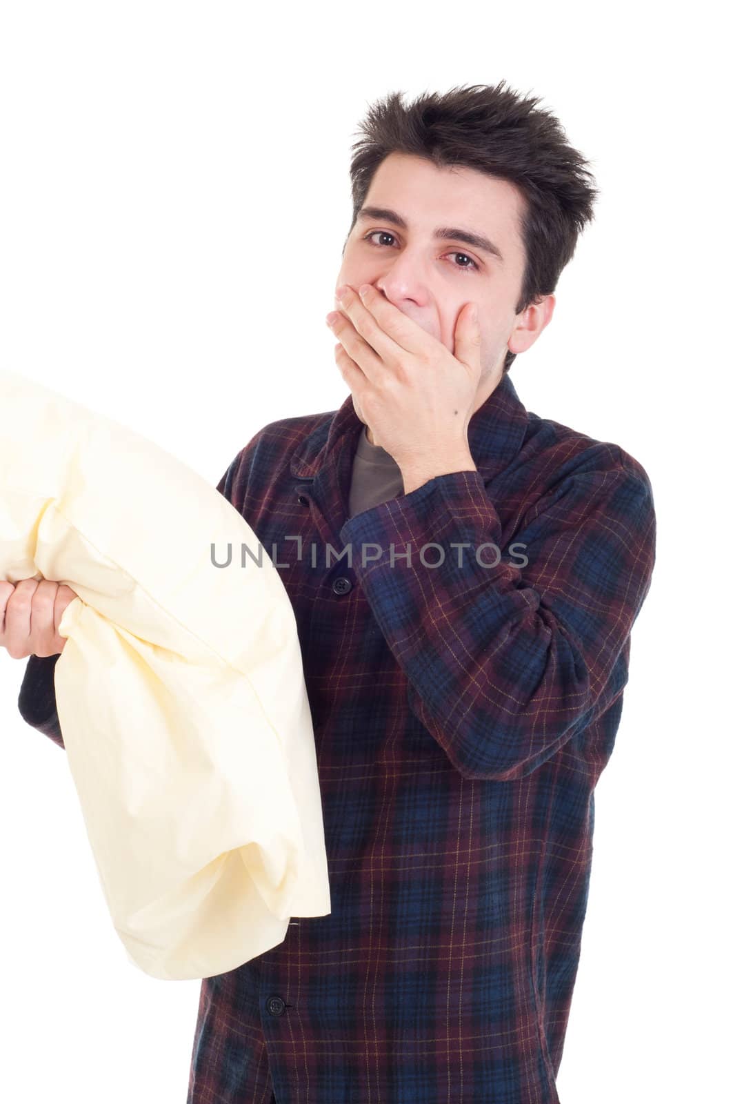 young man in pajamas yawning and holding pillow isolated on white background