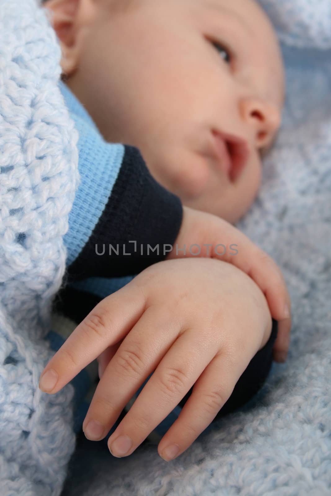 Two month old baby boy wrapped in a blanket. Focus on hand