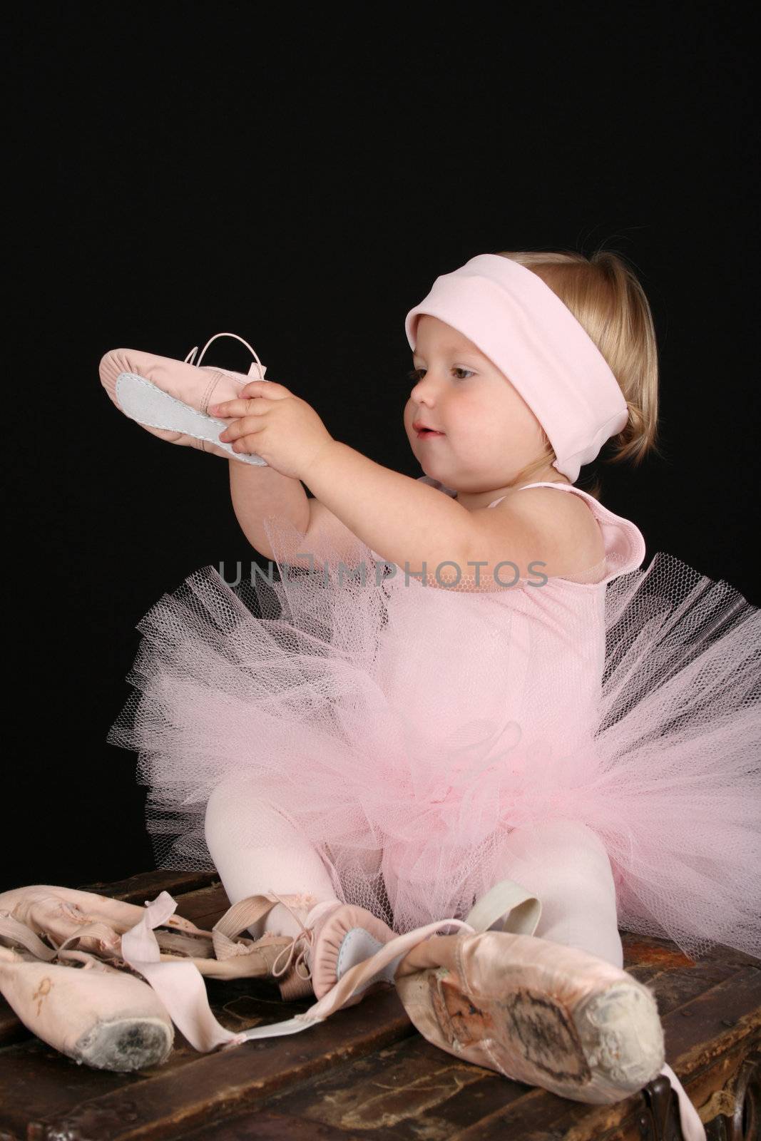Blond toddler wearing a tutu holding Ballet shoes 