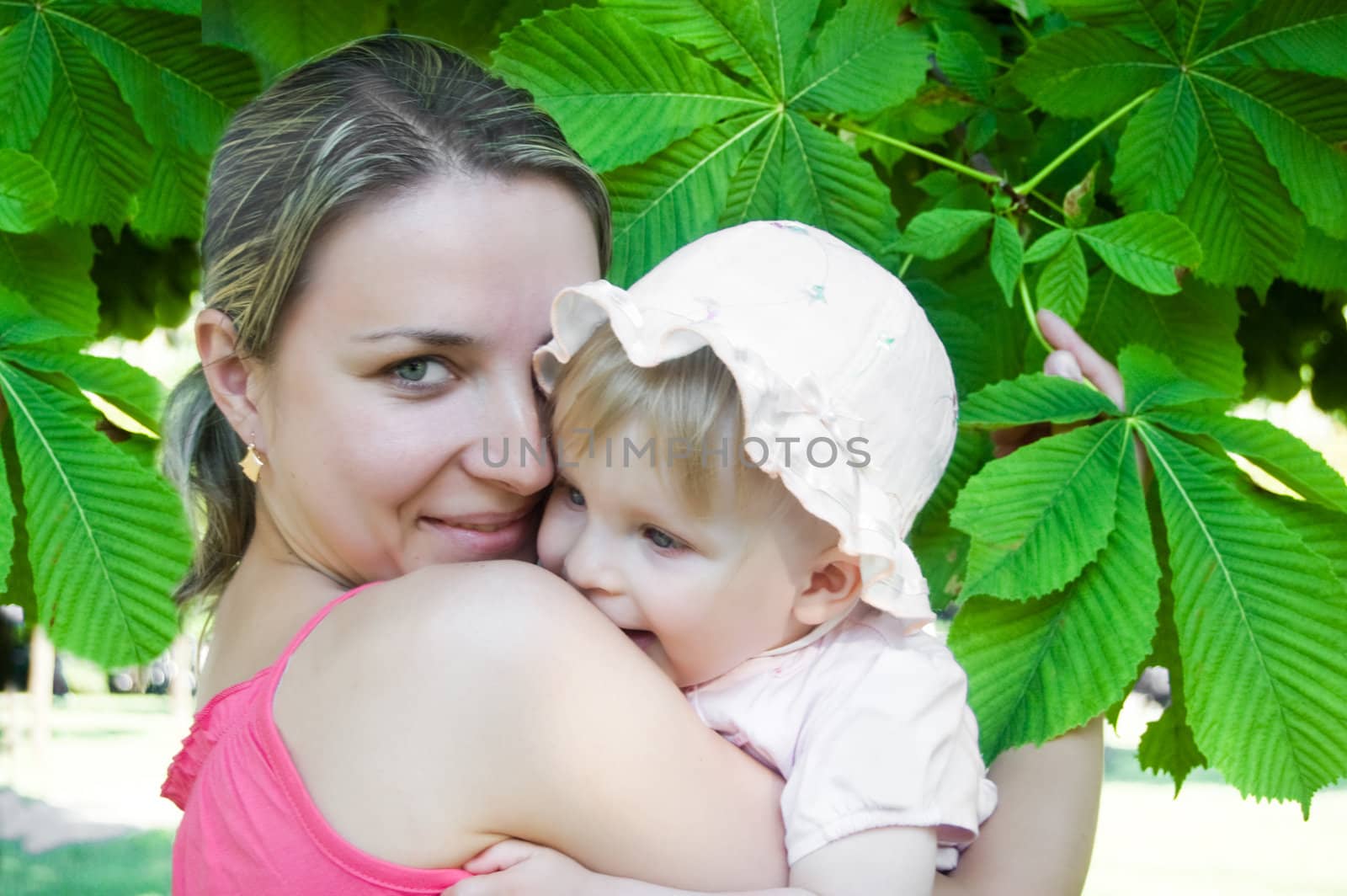 Happy mother and baby girl hugging under tree