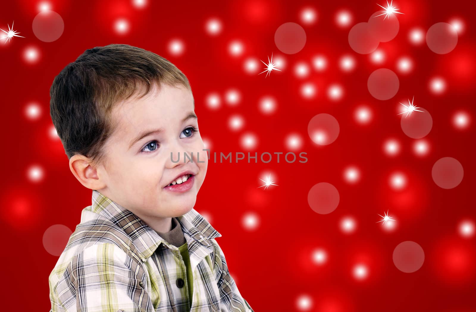 Studio shot of a very cute little boy toddler looking up over bright red Christmas background with bokeh and other light effects.