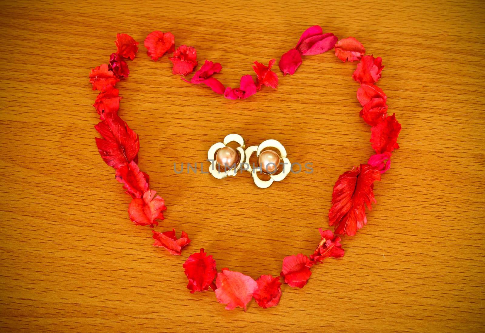Dry flower heart with earrings on wood background
