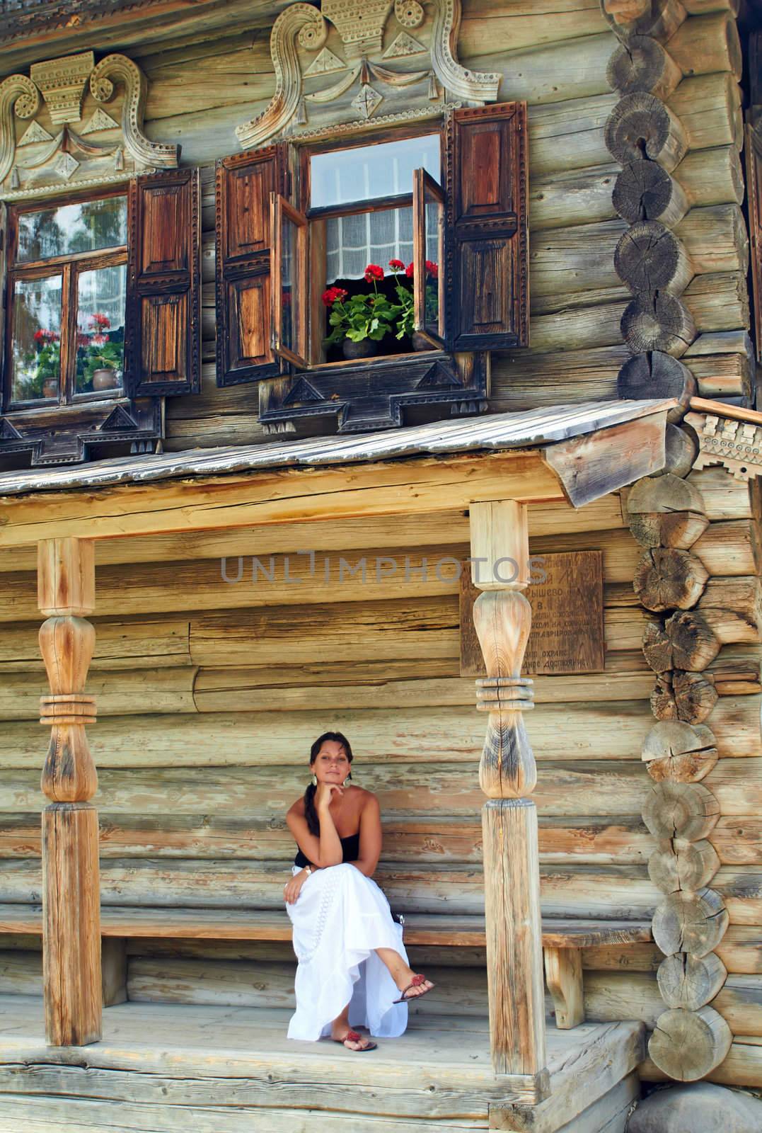Girl sitting on a bench of Old Russian log house