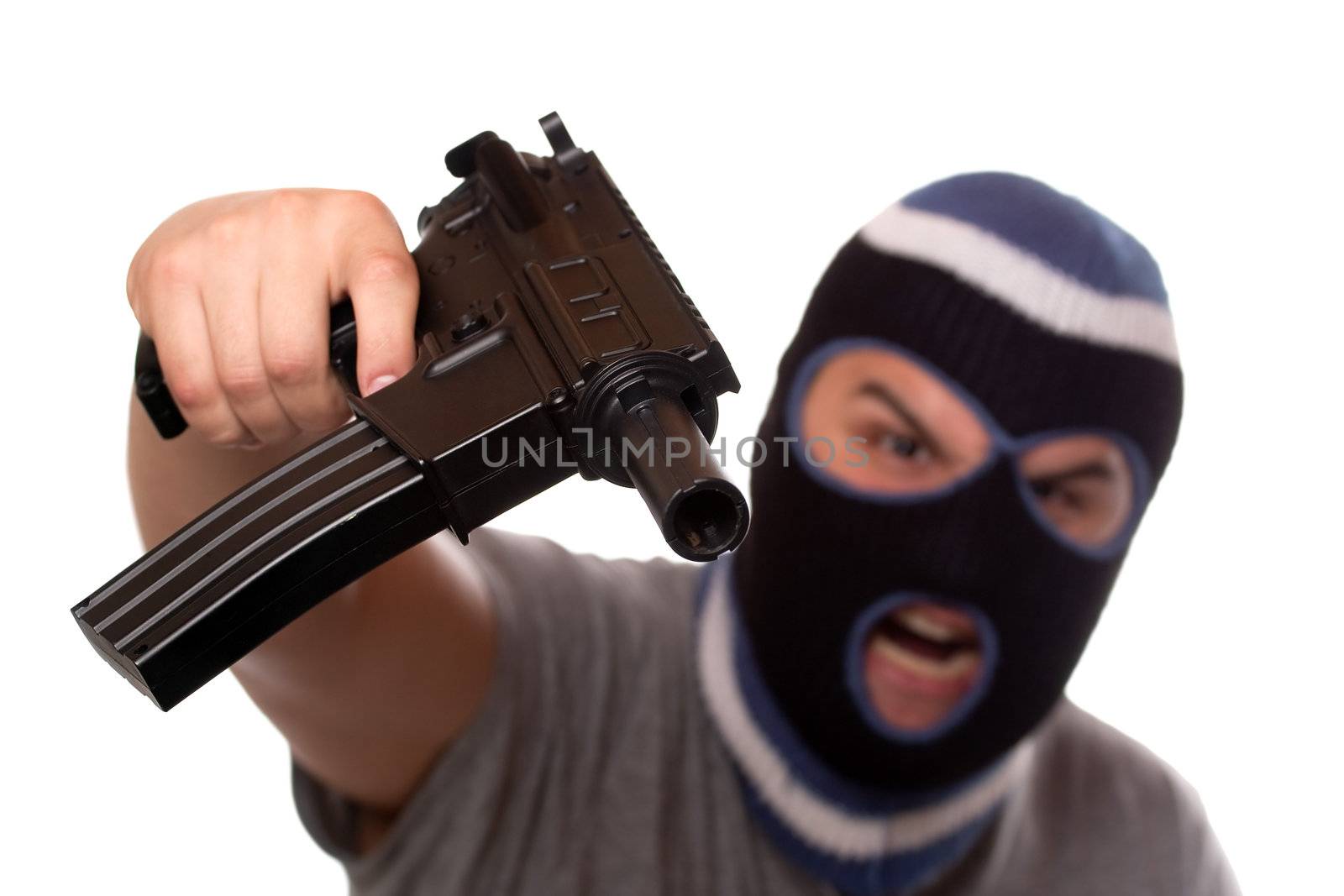An angry looking man wearing a ski mask pointis a black automatic machine gun at the viewer. Shallow depth of field with sharpest focus on the gun.