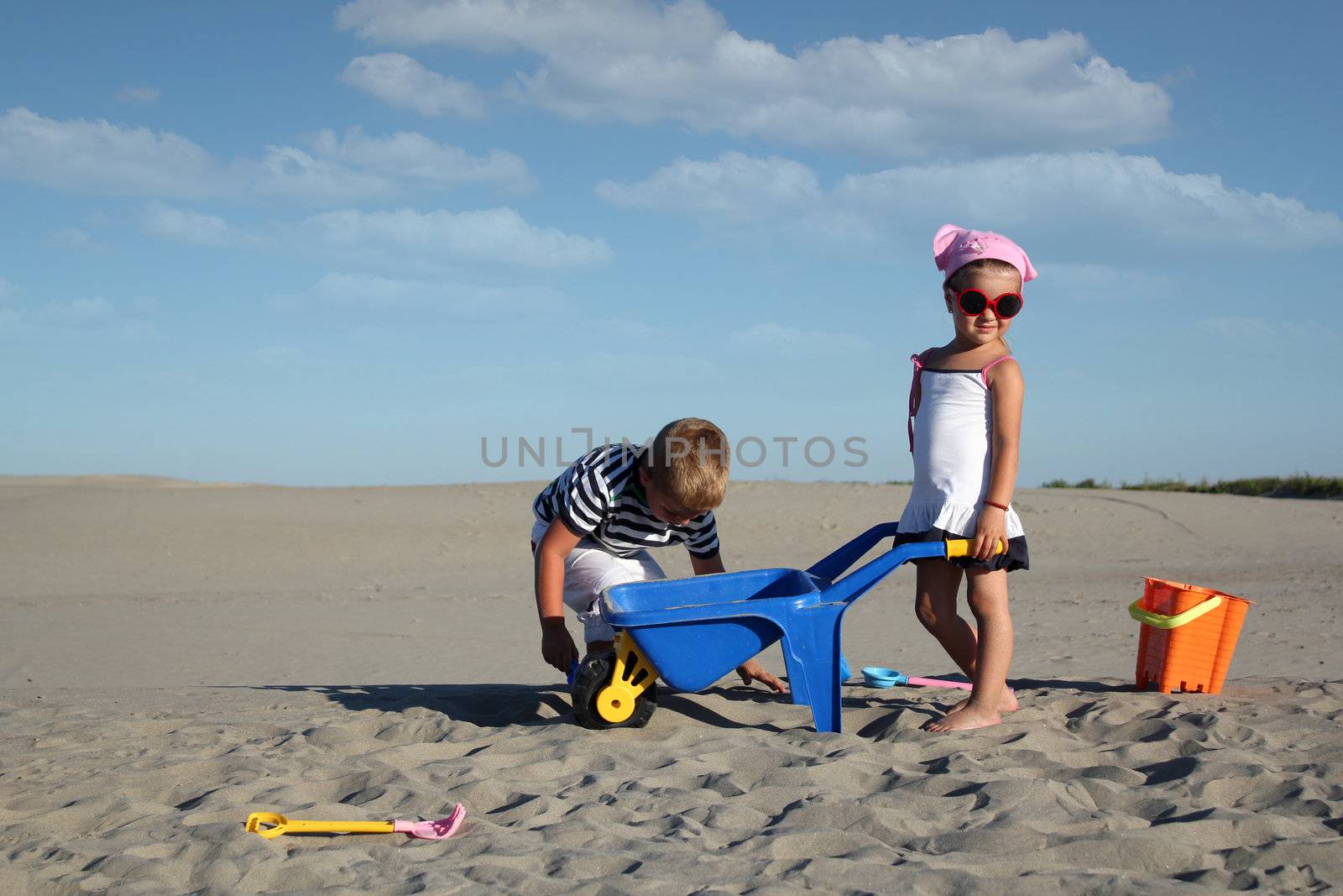 little girl and little boy playing in sand by goce