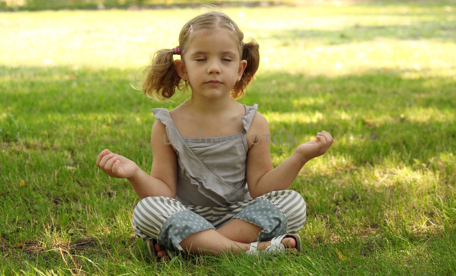 little girl meditating in park by goce