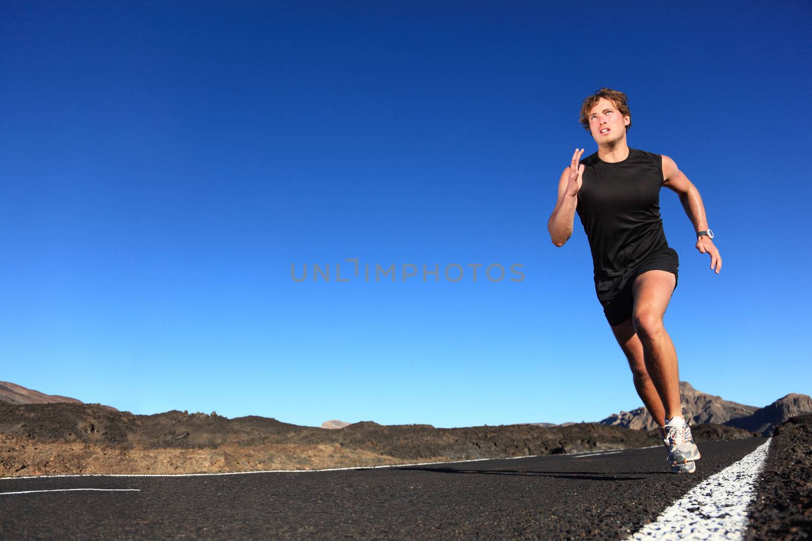 Running man. Male runner at sprinting speed training for marathon outdoors in amazing volcanic dessert landscape. Strong and fit caucasian male fitness model.