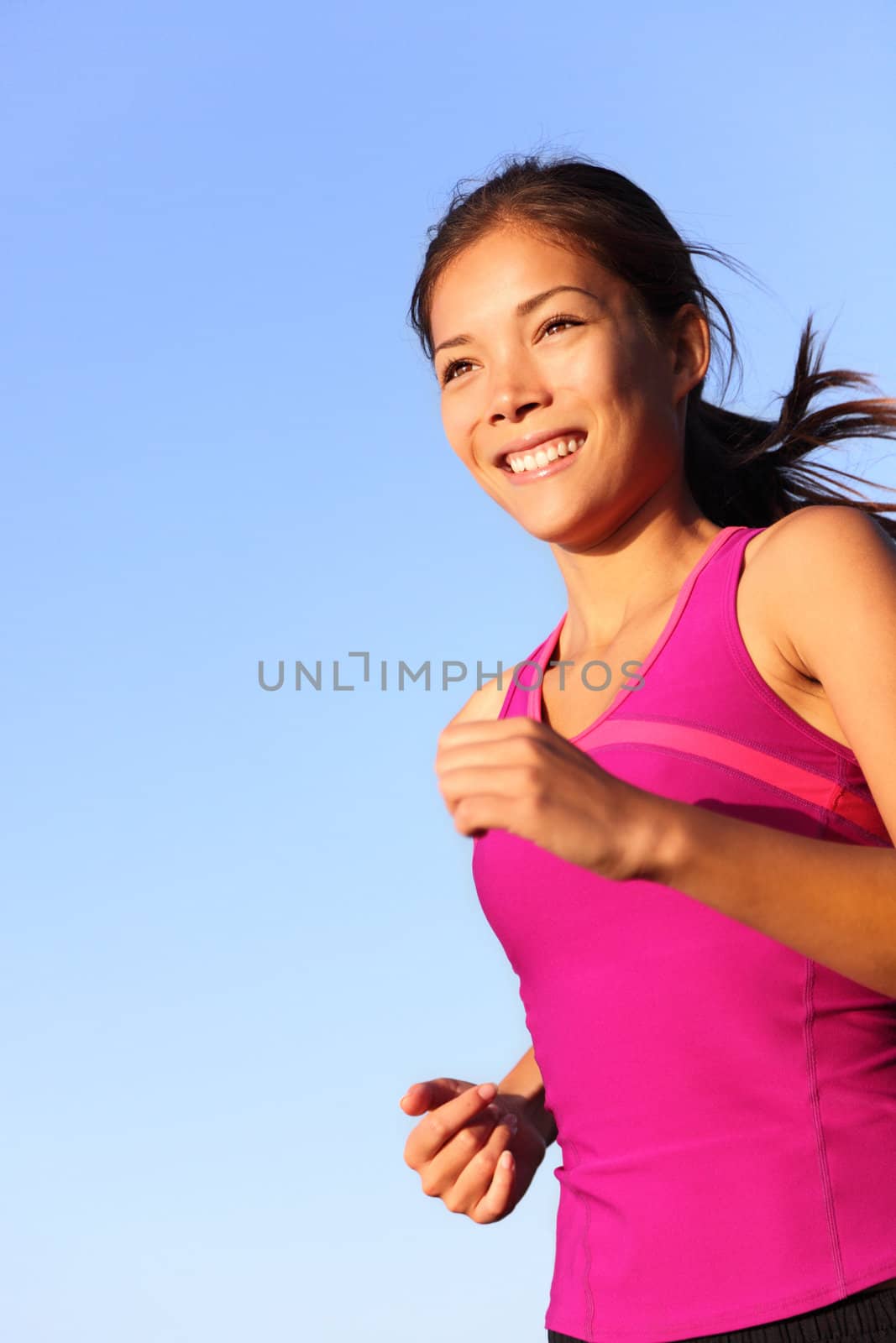 woman running. Female runner jogging outdoors against blue sky. Beautiful healthy and fit young mixed race Caucasian / Chinese Asian fitness model jogging outdoors at sunset.
