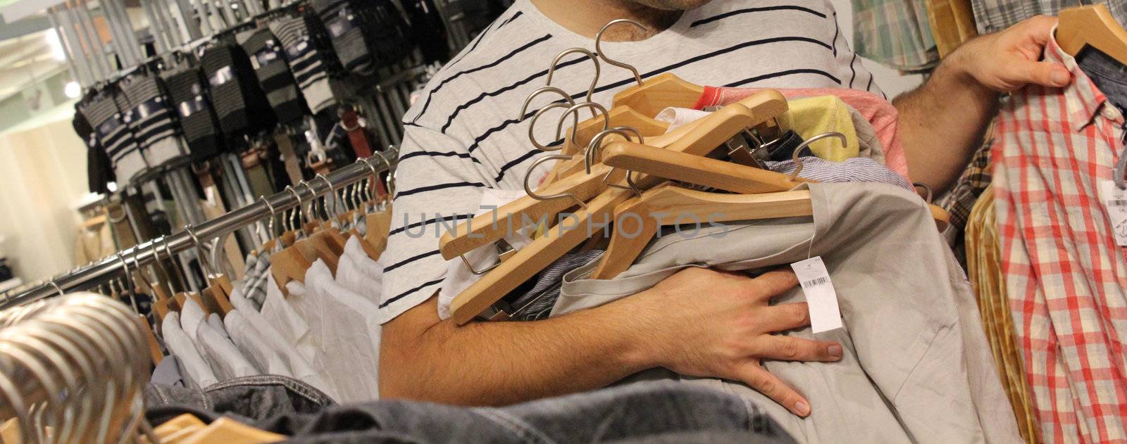 young man clothes shopping with far too many clothes and choices in his hand