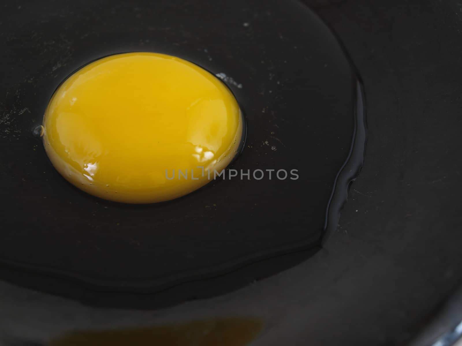 A raw egg cracked on a black plate. Studio isolation.