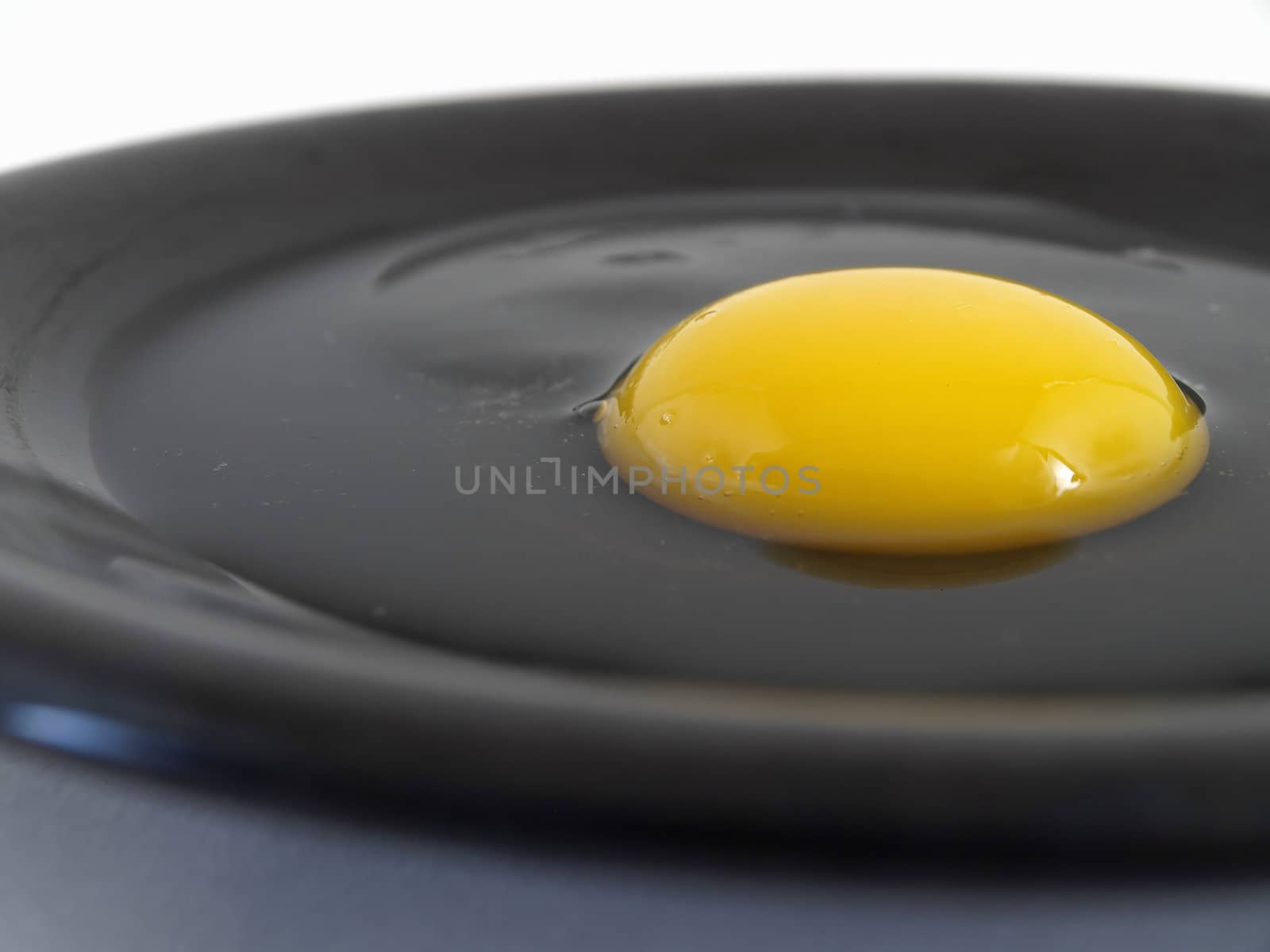 A raw egg cracked on a black plate. Studio isolation.