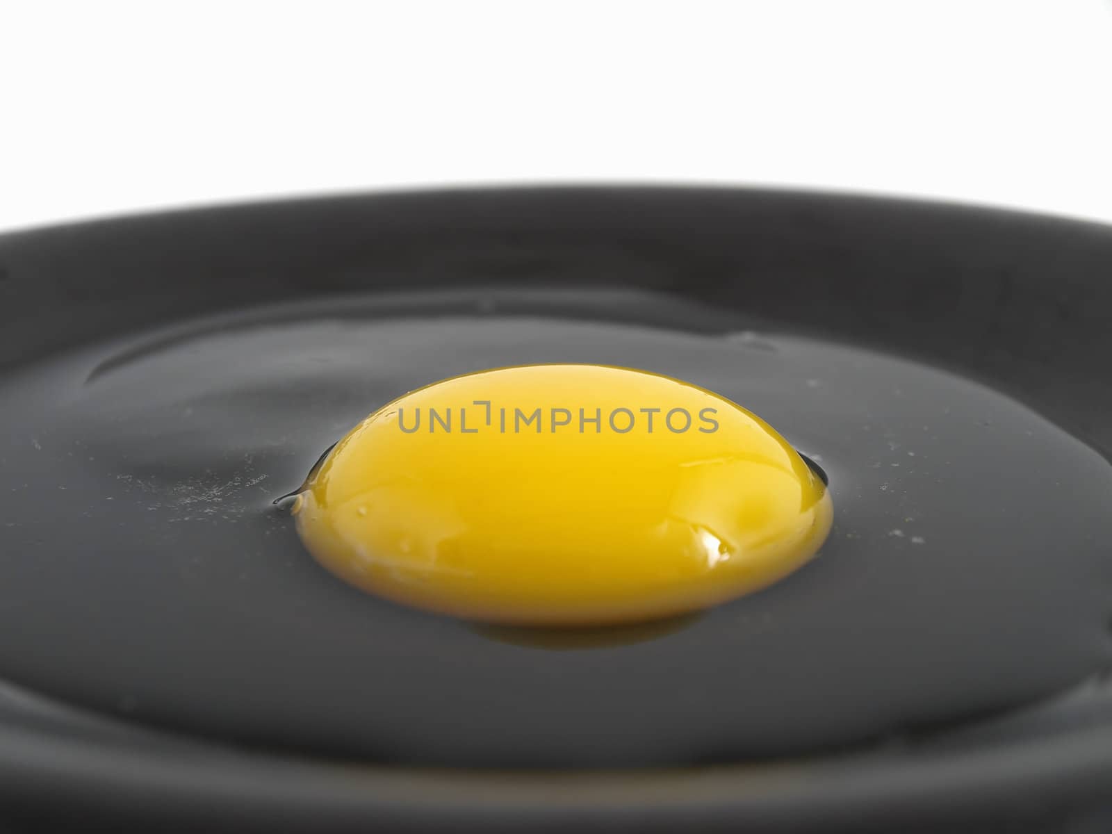 A raw egg cracked on a black plate. Studio isolation.