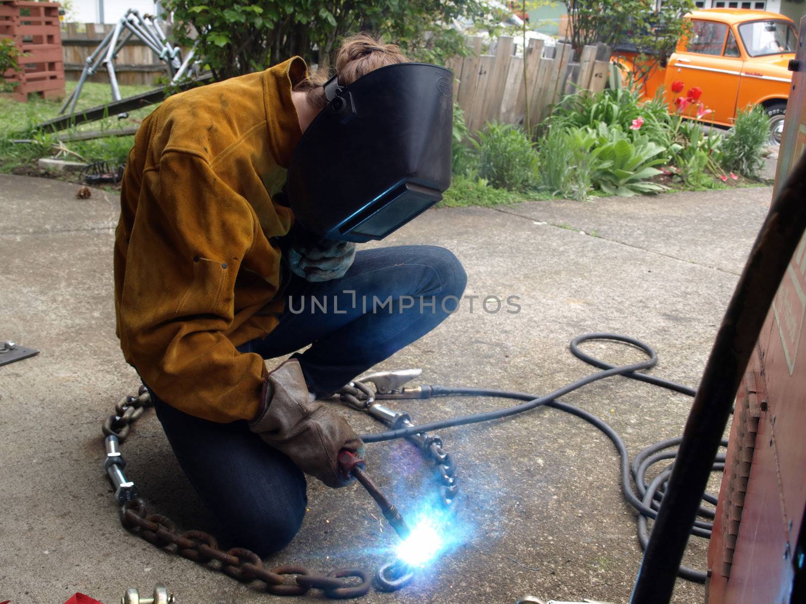 A woman wearing protective gear welds a piece of chain together.