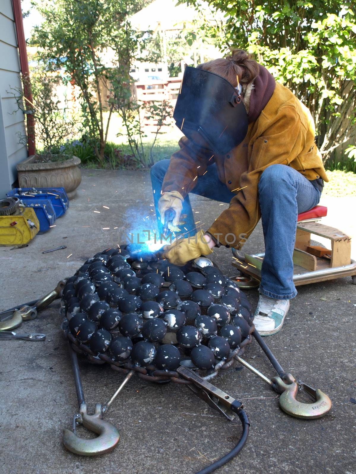A woman wearing protective gear welds a metal art sculpture together.
