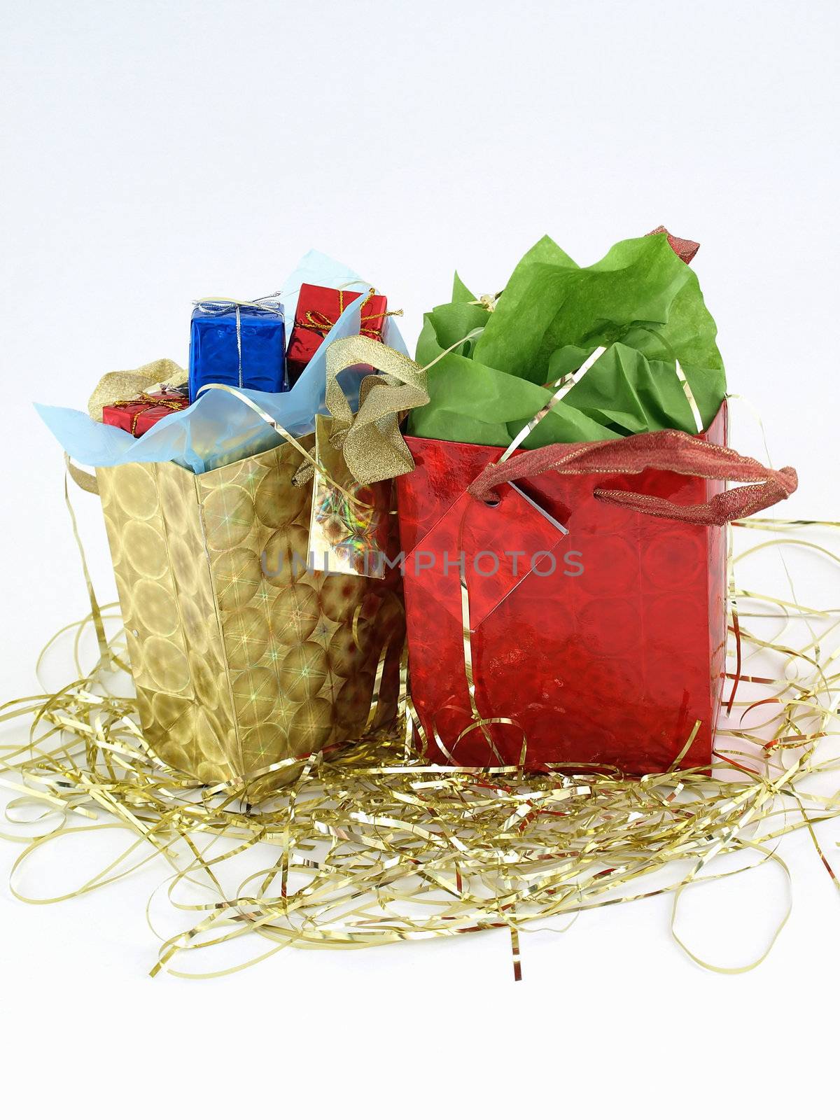 Two foiled gift bags full of wrapped presents. On a bed of gold tinsel over a white background.