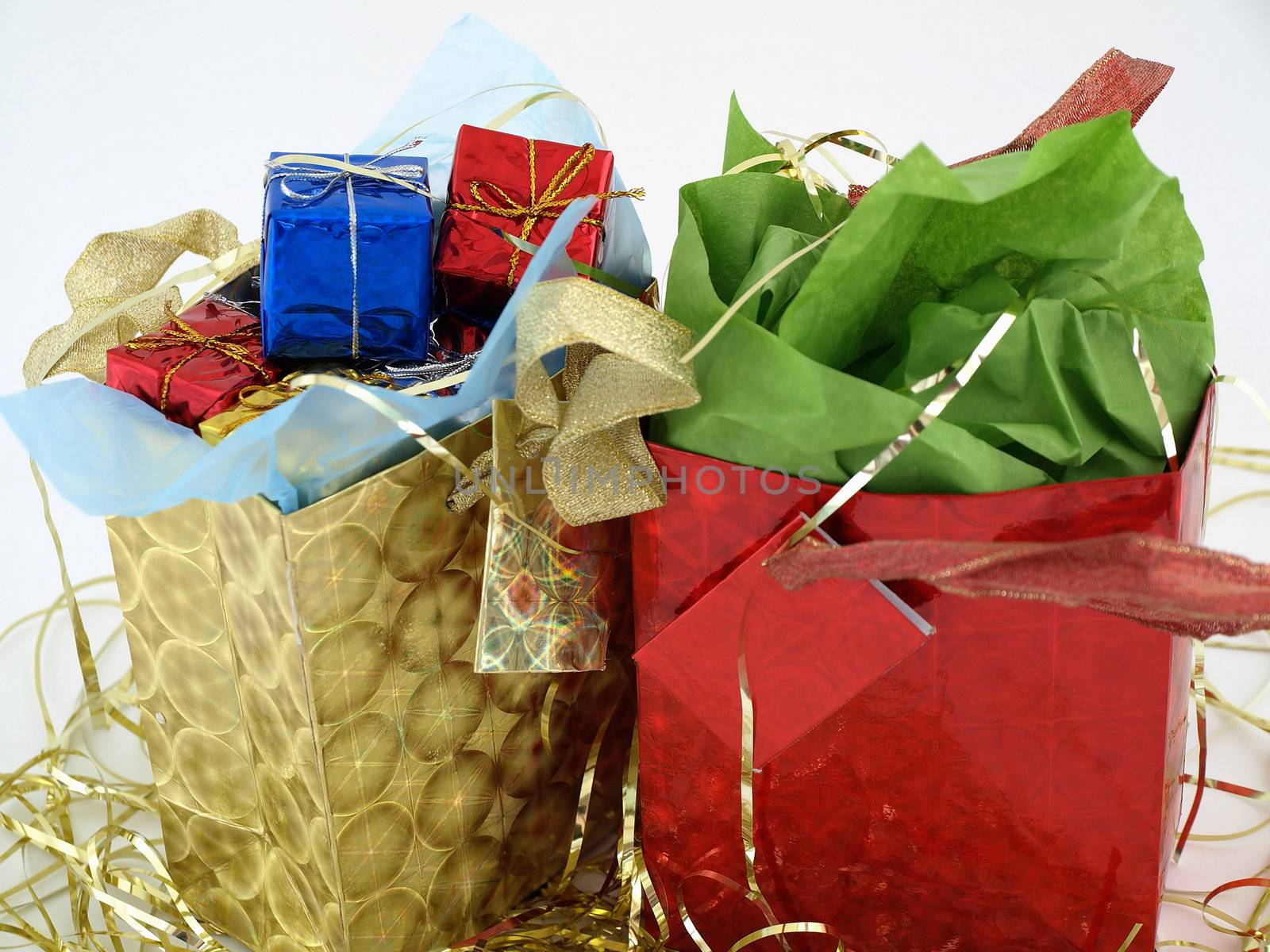 Two foiled gift bags full of wrapped presents. On a bed of gold tinsel over a white background.