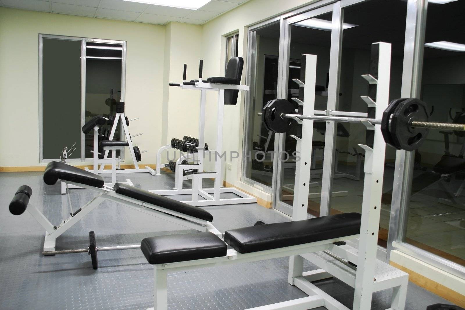 exercise gym with various benches dumb bells and bars
