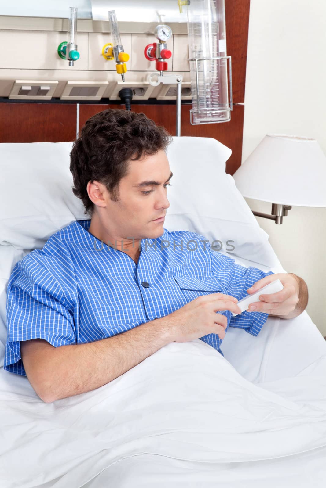 Young patient sitting on bed reading medicine box in hospital