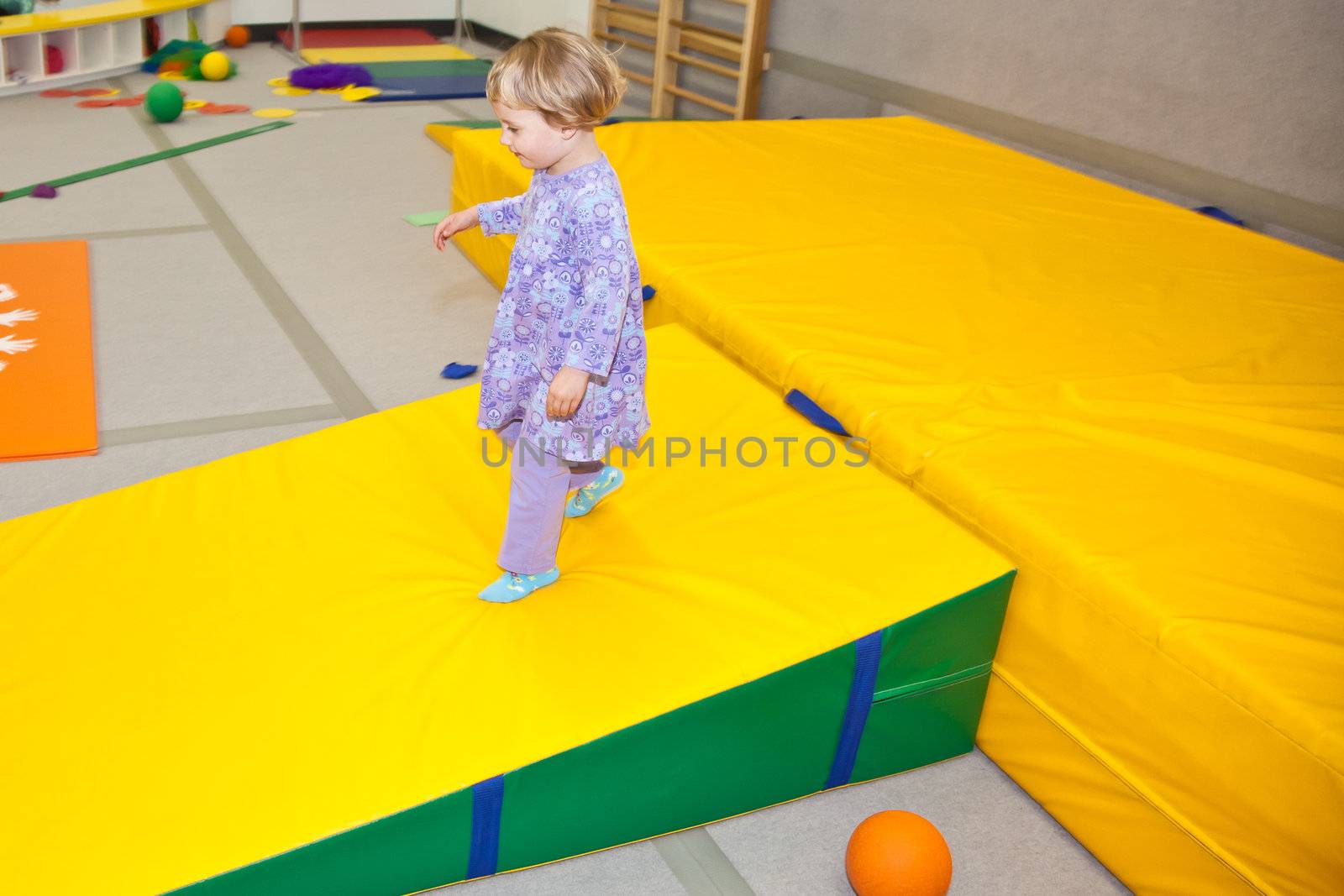 Cute little European toddler girl having fun at indoor playground.