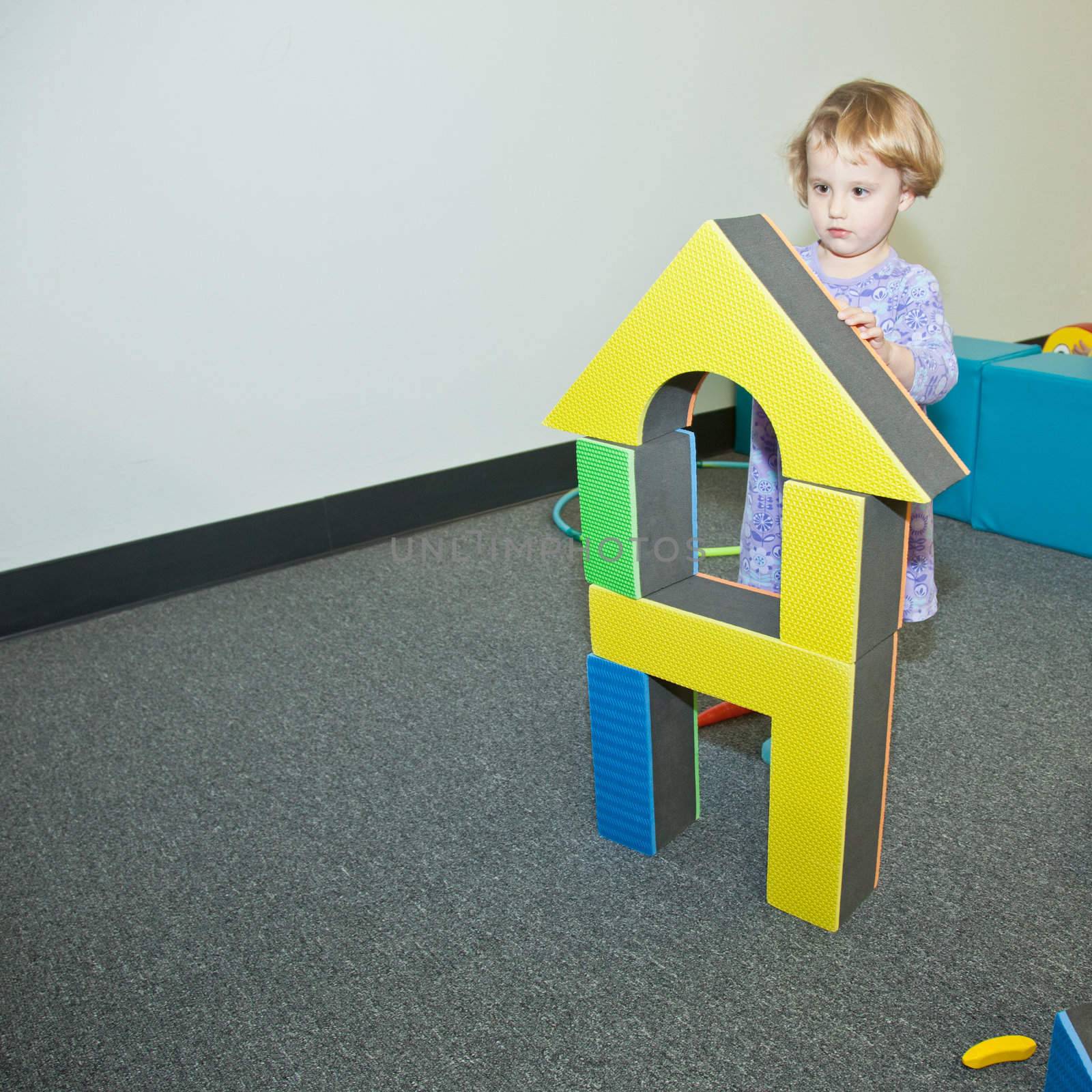 Cute little European toddler girl having fun at indoor playground.