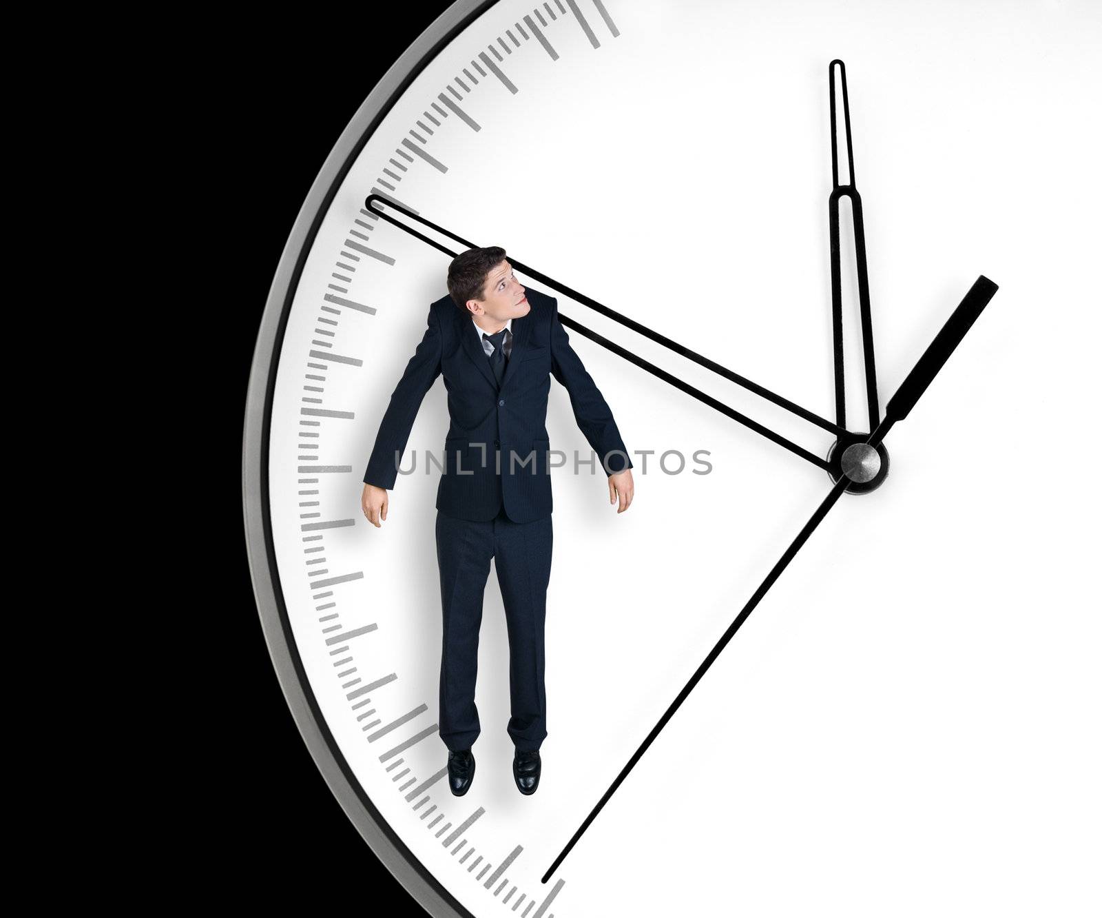 Businessman hangs on an arrow of clock, isolated on black background