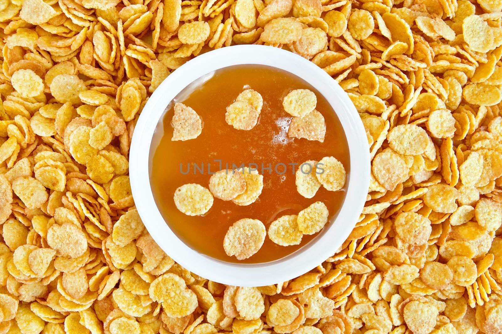 Honey in a white cup on the background texture of golden corn flakes
