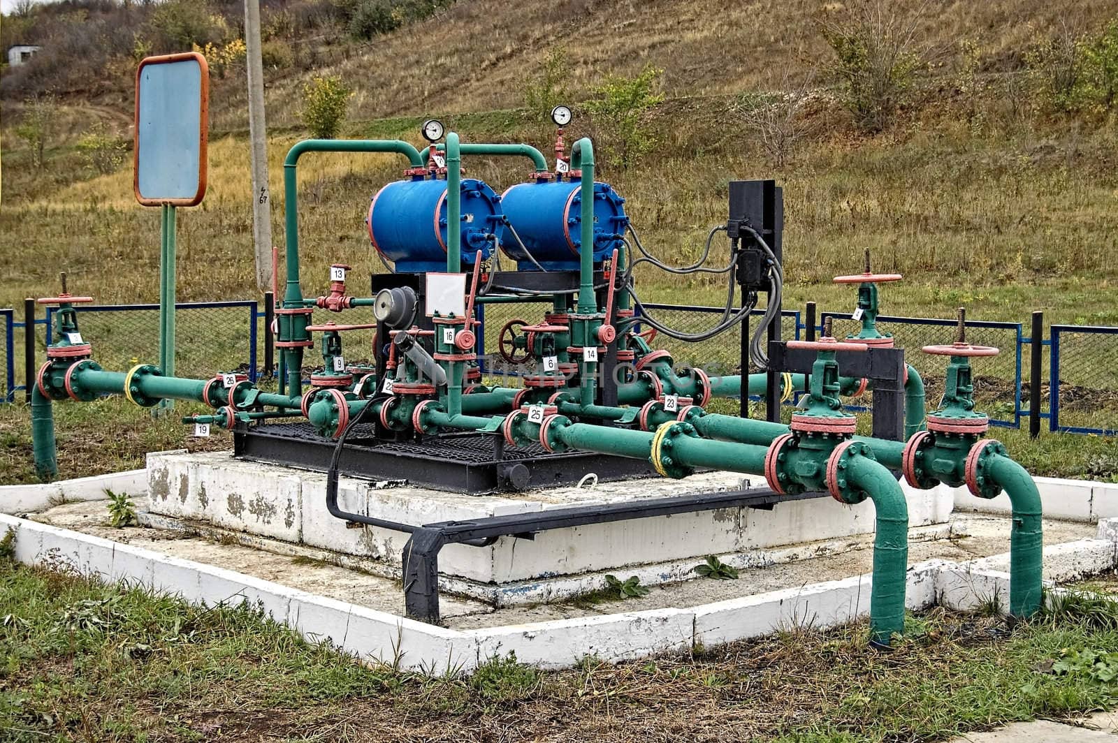 Blue cylinders, green with red edging pipe group metering device of the pipeline on the black and white based on the background of yellow-green grass and bushes