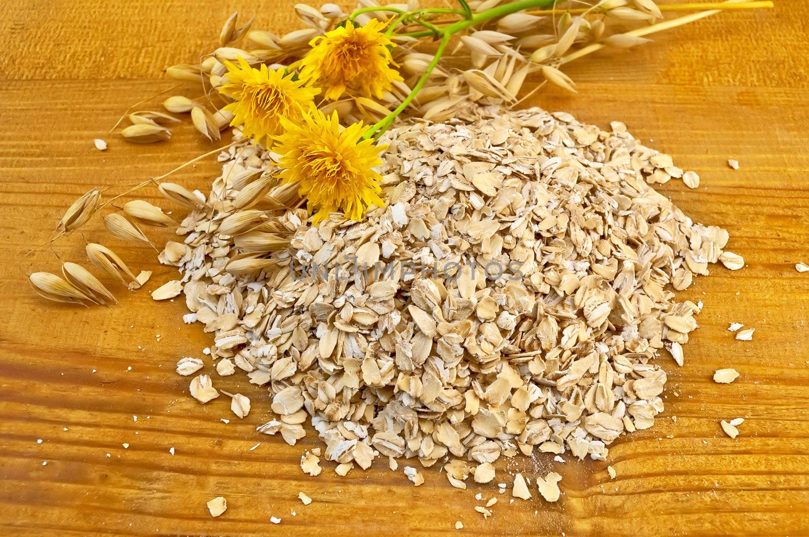 Oatmeal with yellow wild flowers and stalks of oats against a wooden board
