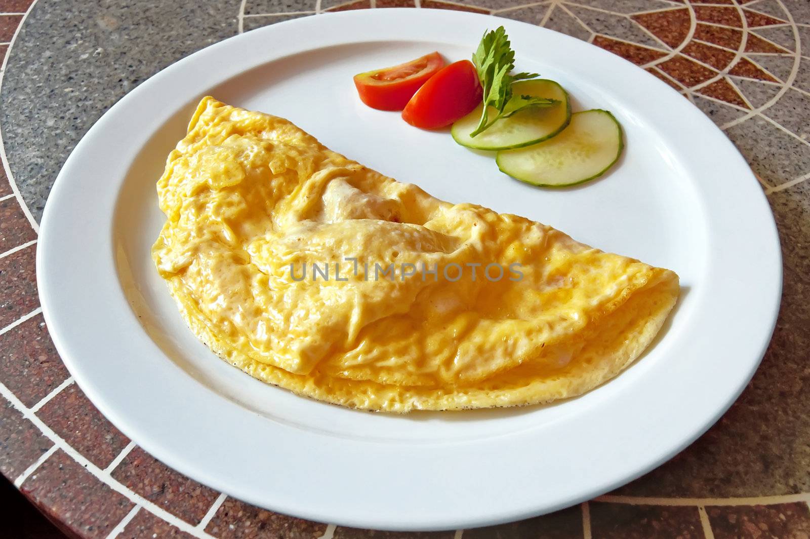 Yellow omelet, two slices of red tomatoes and cucumber, a sprig of parsley on the plate against the backdrop of granite countertops with a pattern