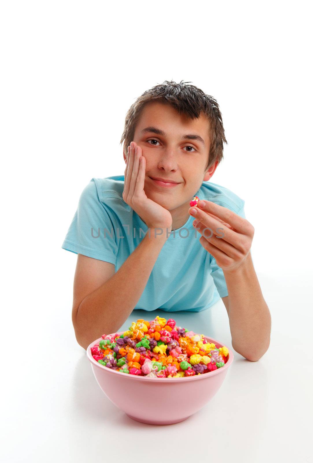 A boy relaxing with a large bowl of colourful popcorn.  White background.