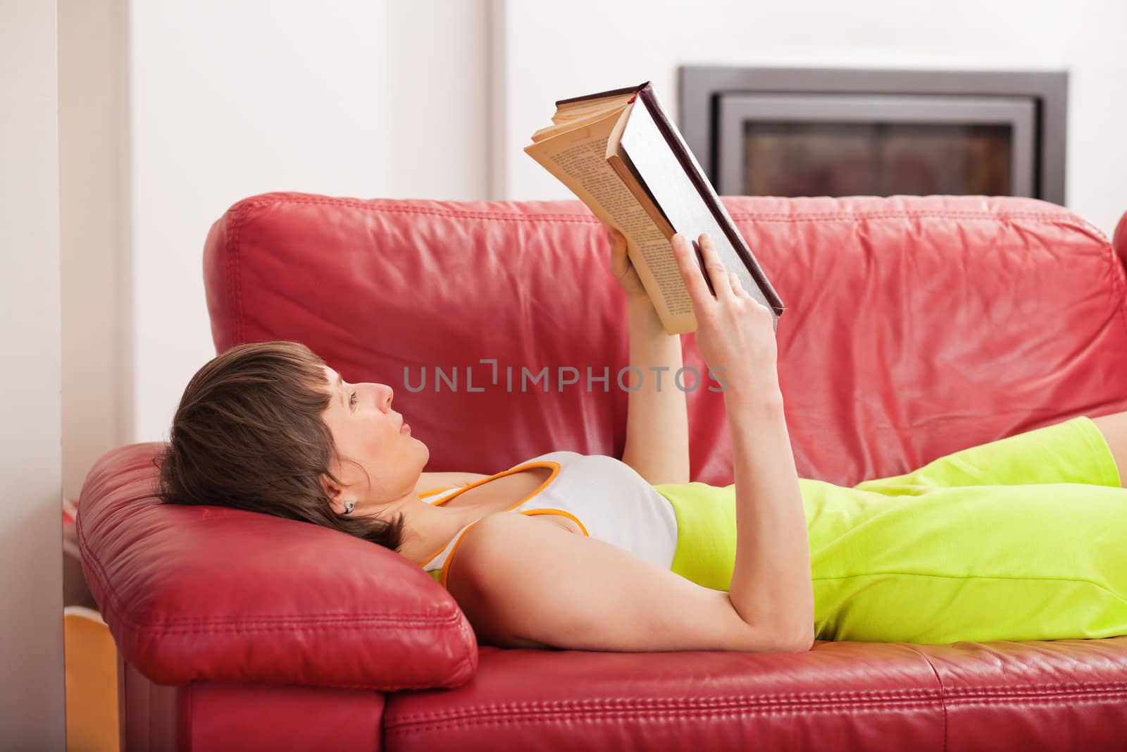 Woman lying on the couch and reading a hardcover book