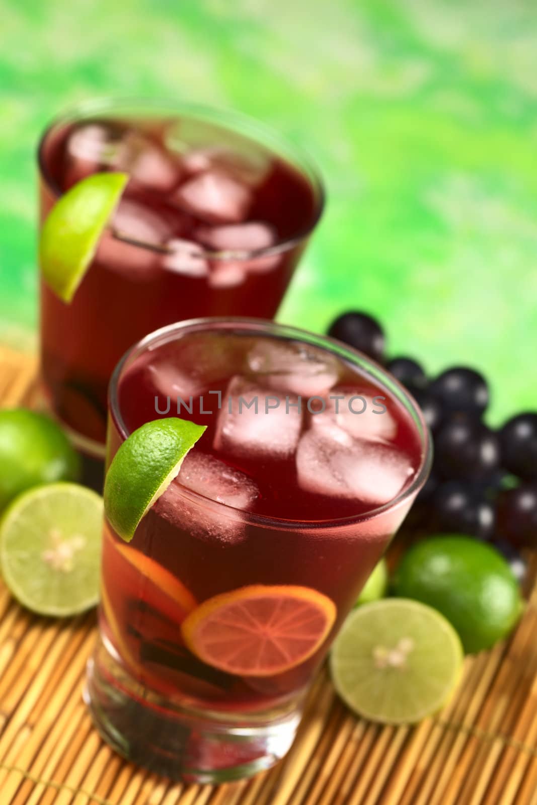 Refreshing red grape lemonade consisting of red grape and lime juice and ice cubes (Selective Focus, Focus on the front rim of the first glass and the front of the lime wedge on the rim) 