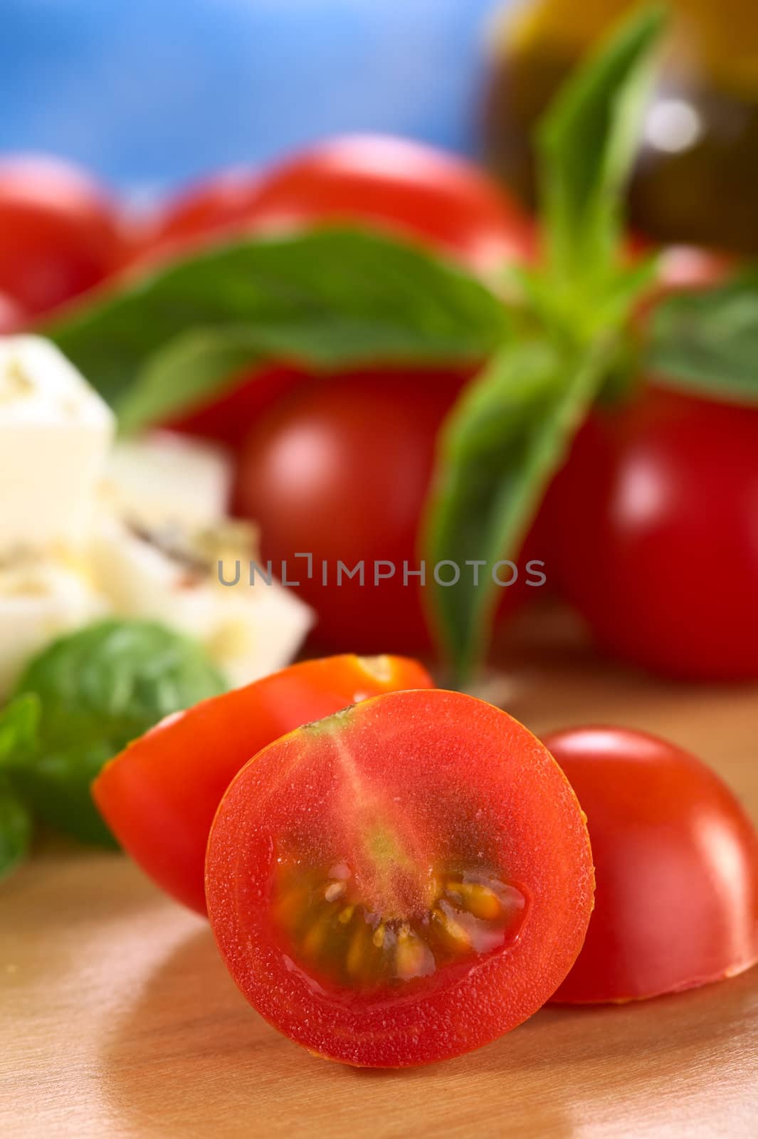 Raw cherry tomato cut in half with cheese and basil in the back (Selective Focus, Focus on the surface of the cut tomato)