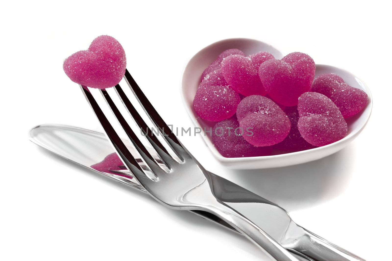 Pink heart shaped jelly sweets with knife and fork on white background