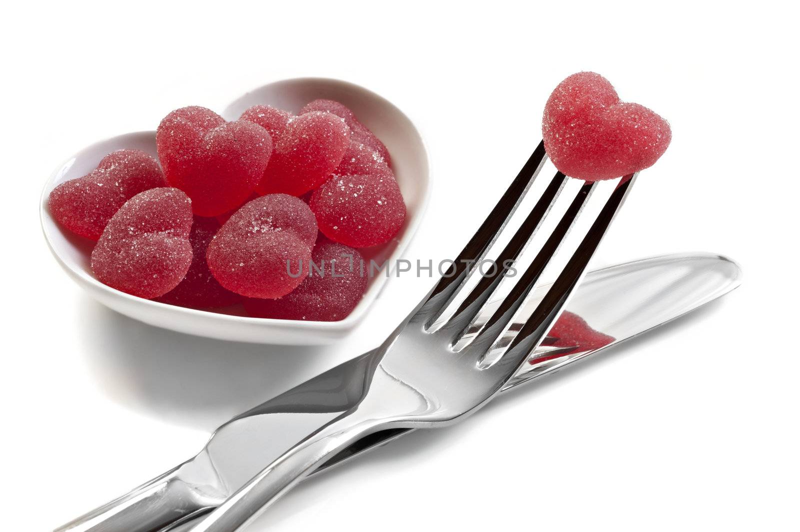 Red heart shaped jelly sweets with knife and fork on white background