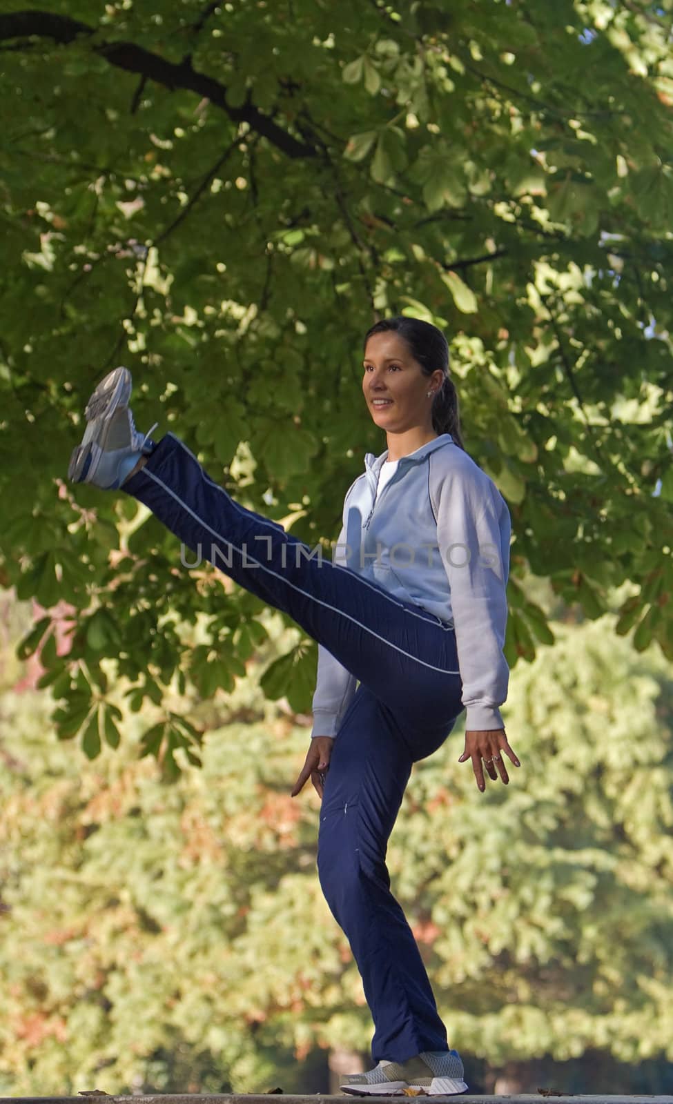 Young woman doing warming up movements outdoors under a tree.Shot with Canon 70-200mm f/2.8L IS USM